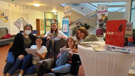 Fünf Schülerinnen sitzen zusammen und arbeiten an einem Fairtrade-Projekt.